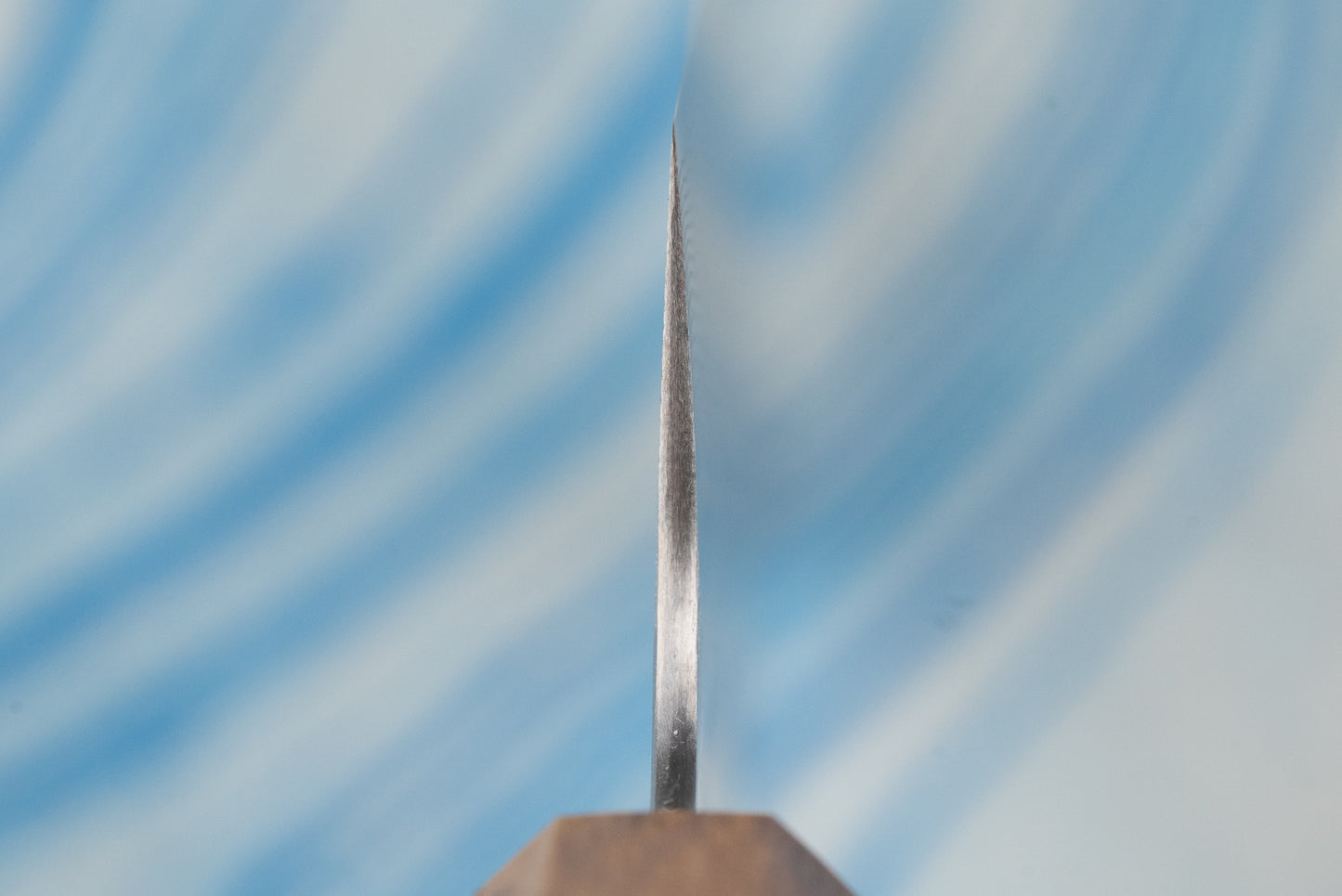 Extreme close-up of the sharpened cutting edge of a Nigara SPG STRIX Tsuchime Damascus Nakiri 180mm, showcasing its precision craftsmanship, with a hint of the wood-toned handle visible.
