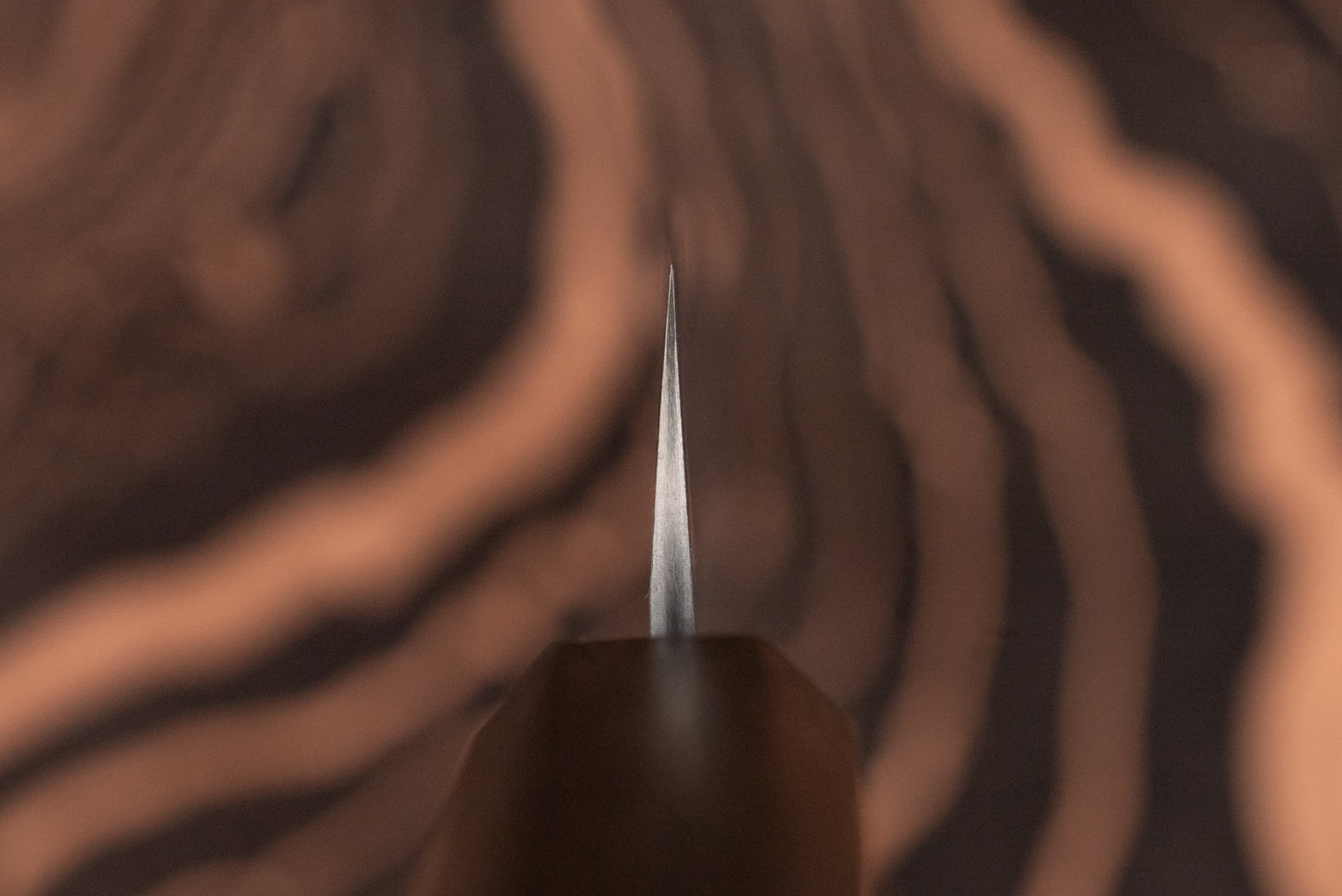 Nigara VG XEOS Tsuchime Damascus Petty 160mm knife with a wooden handle, showcasing a sharp metal blade tip against a blurred wood-grain background, ideal for precise cutting tasks.
