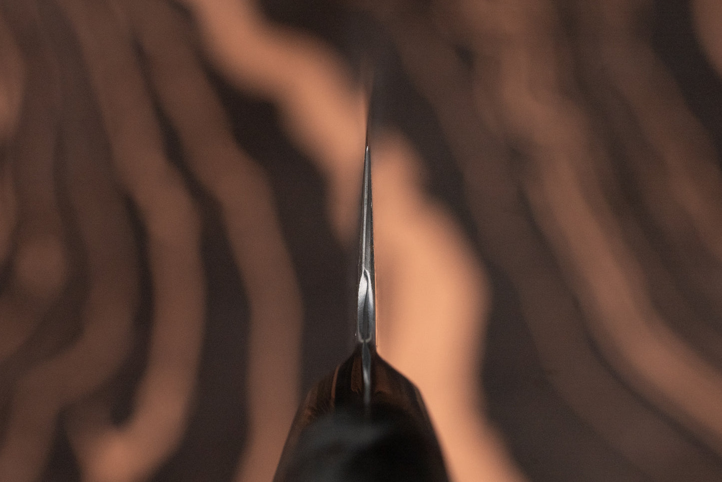 Close-up of the Ryusen Oukokuryu Petty 135mm knife blade, showcasing its sharp edge against a blurred wood-grain background. Ideal for precise cutting tasks, embodying exquisite Japanese craftsmanship.