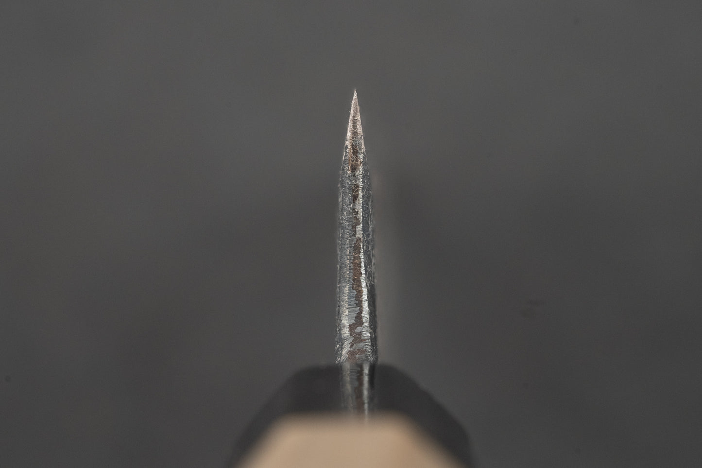 Macro view of the Shiro Kunimitsu Aogami Kurouchi Chikuzen Ko-Bunka 140mm knife tip, showcasing its robust bevel and slightly visible handle, epitomizing Japanese craftsmanship in kitchen knives.