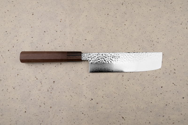 The Touroku Sakai Yukage Nakiri 160mm rests on a speckled counter, showcasing its straight rectangular blade with hammered and Damascus patterns, paired with a traditional dark wooden octagonal handle.