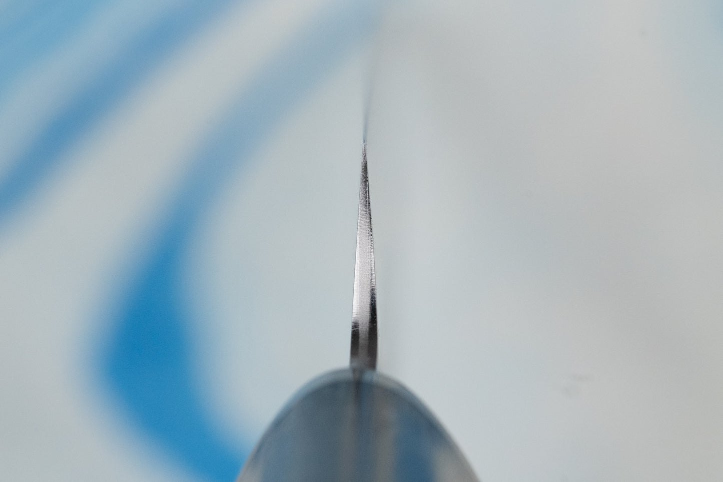 Touroku Sakai Gekka Petty 120mm knife, seen edge-on in a macro view, showcasing its razor-sharp VG10 stainless steel blade, ideal for precise cutting tasks on a board.