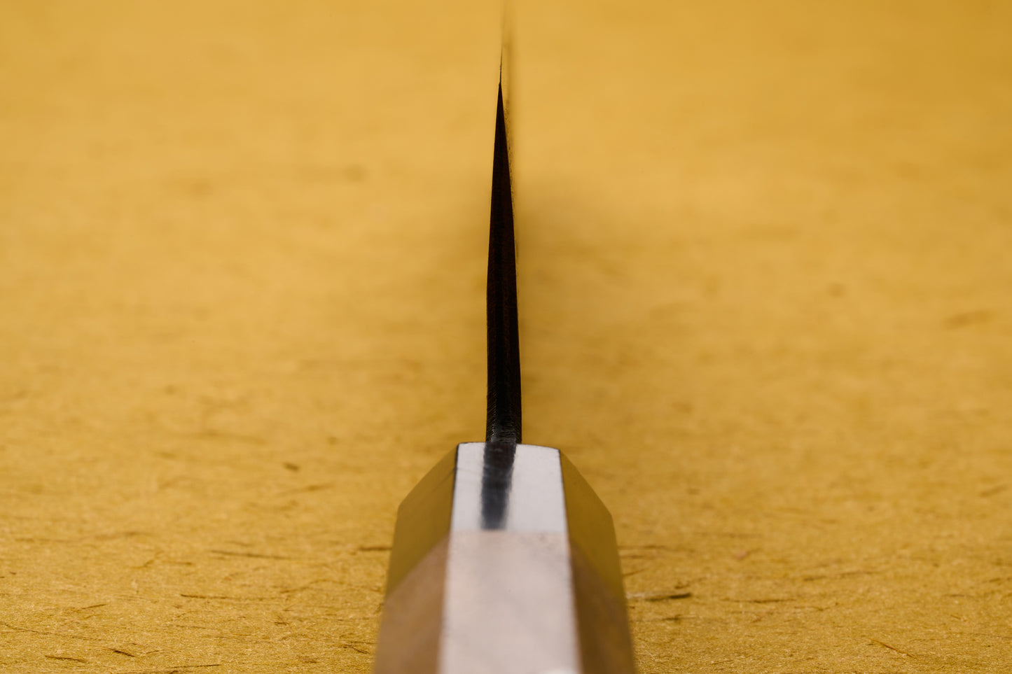 Tight shot of Touroku Sakai Yoshikazu Shirogami Kurouchi Gyuto 240mm blade, showcasing the sharp edge against a pale surface, embodying the traditional European chef knife profile with Japanese craftsmanship.