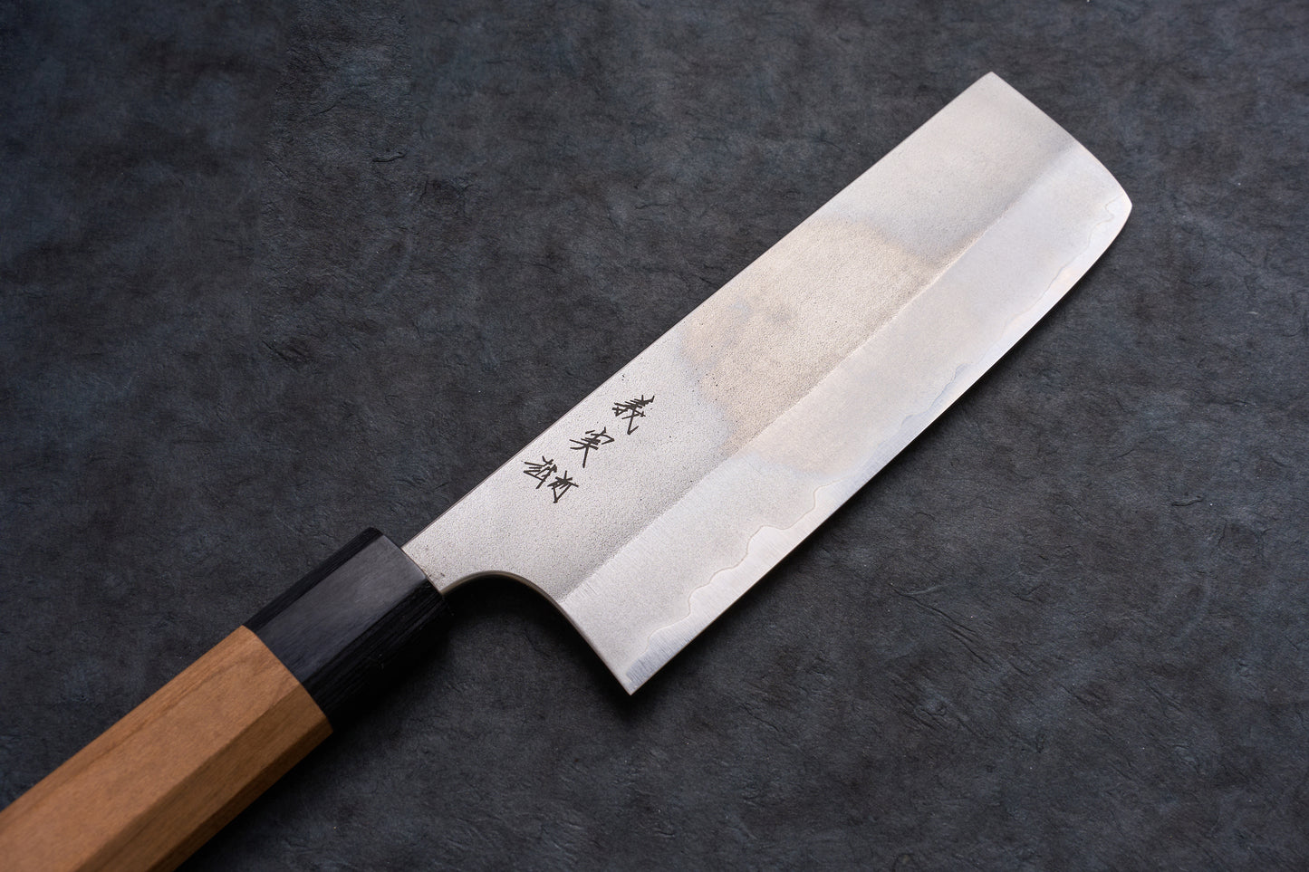 Yoshimi Kato AS/S Nashiji Nakiri 165mm knife, featuring a straight steel blade with hamon and kanji, and an octagonal wooden handle, displayed on a dark surface.