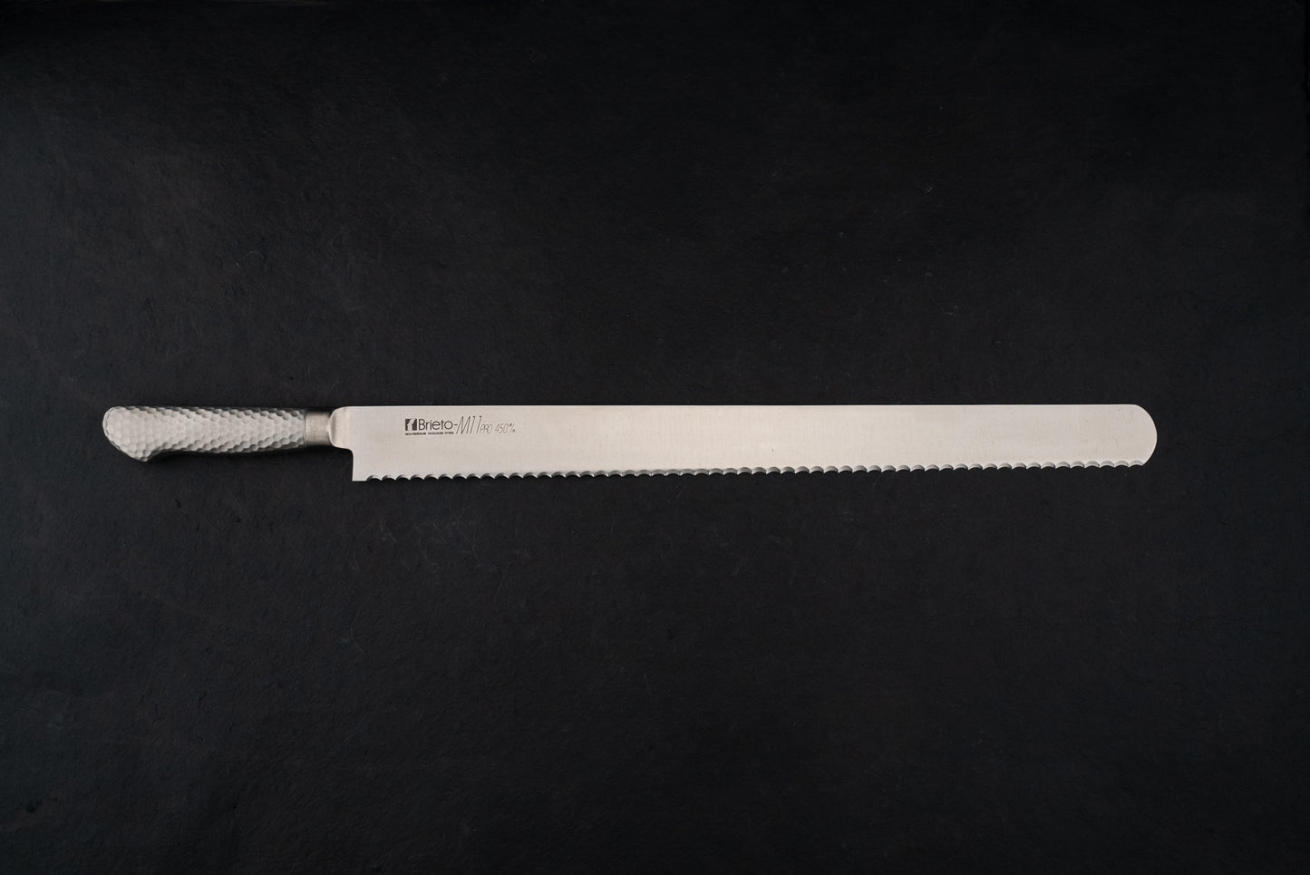 Brieto Pro Bread Knife 450mm M1146 with a hammered metal handle and extra-long serrated blade, ideal for precise slicing, showcased against a dark backdrop, embodying Knifewear's dedication to unique Japanese craftsmanship.