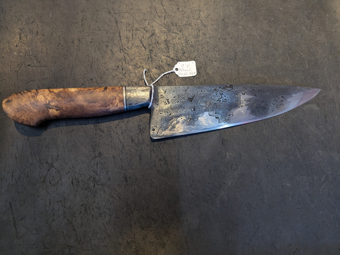 Black Cat Metal Damascus San Mai Chef knife with patterned blade and spalted maple handle, featuring alloys 80CrV2, 15N20, and 1084, on a scratched surface.