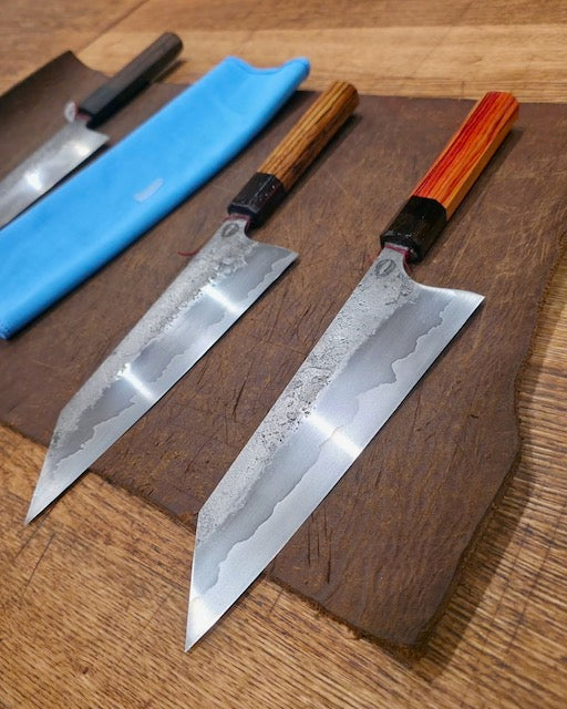Bad Llama Forge Bunka 195mm knives feature laminated blades and turned wooden handles, embodying Japanese artistry and Canadian craftsmanship. Displayed on a board with sleek, sharp lines and unique handle tones.