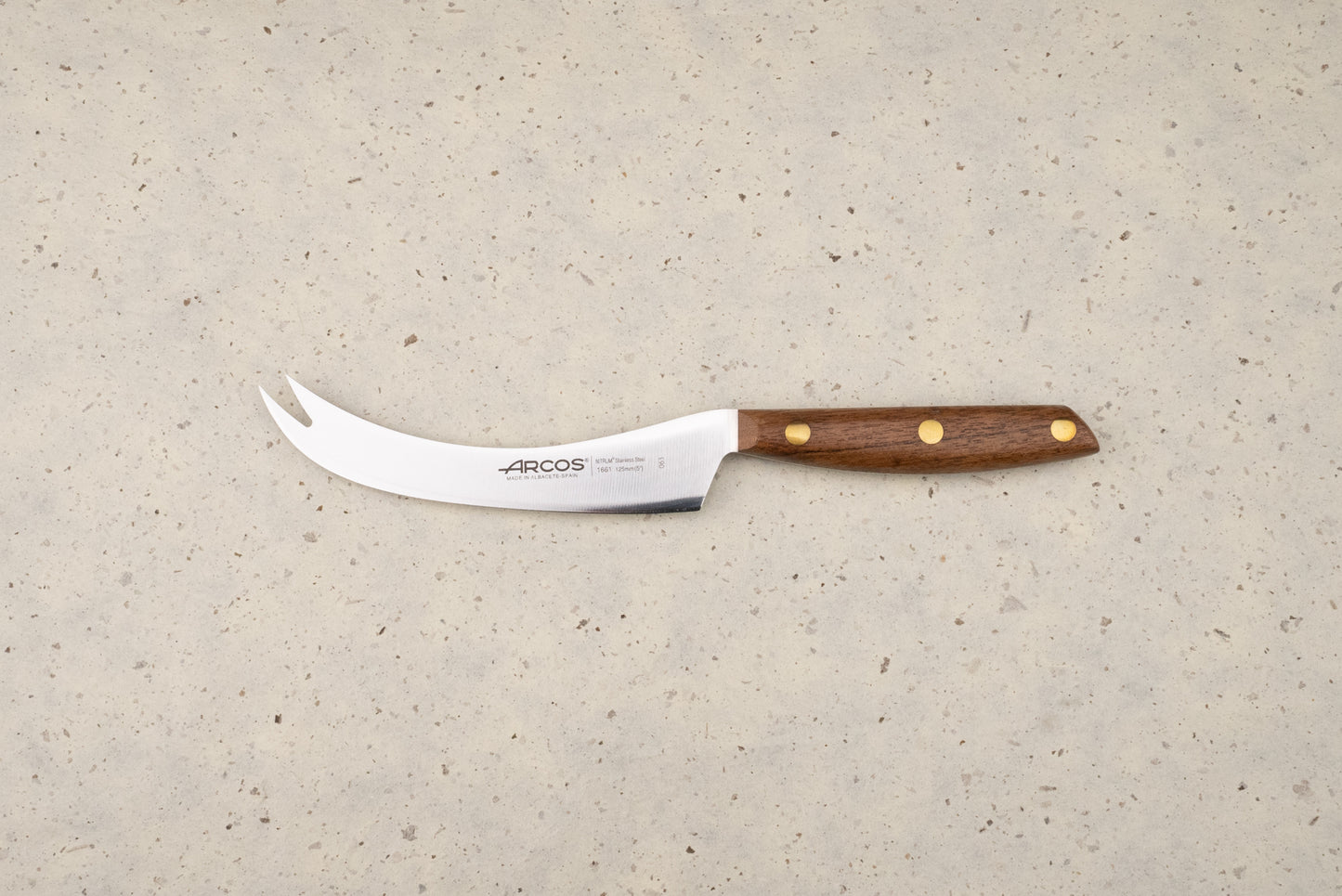 Arcos Nordika 125mm Manchego Knife features a curved blade with a two-pronged tip, perfect for slicing cheese. Its wooden handle and three-rivet construction showcase craftsmanship from Albacete, Spain.