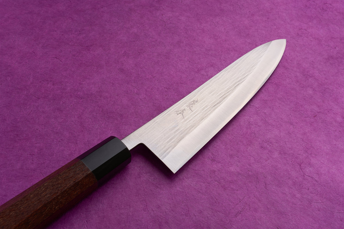 Fujimoto AS Sazanami Gyuto 210mm knife with a hammered steel blade and etched characters, featuring a dark wood octagonal handle on a purple background.