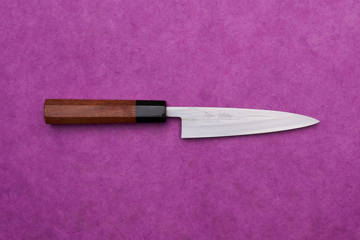 Fujimoto AS Sazanami Petty 135mm knife with octagonal wooden handle on a purple background, showcasing its sleek design and high-performance craftsmanship.