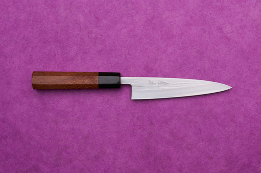 Fujimoto AS Sazanami Petty 135mm knife with octagonal wooden handle on a purple background, showcasing its sleek design and high-performance craftsmanship.