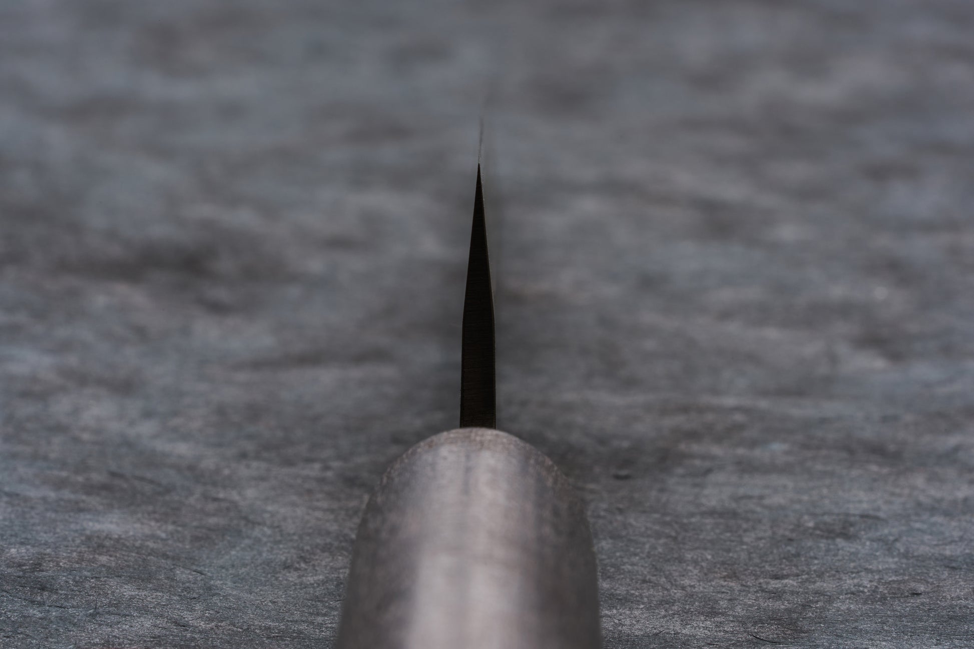 Close-up of the Fujimoto Nashiji Petty 135mm knife blade edge, showcasing its sharp carbon steel core and protective stainless steel layer, with a blurred handle foreground, ideal for precise cutting tasks.
