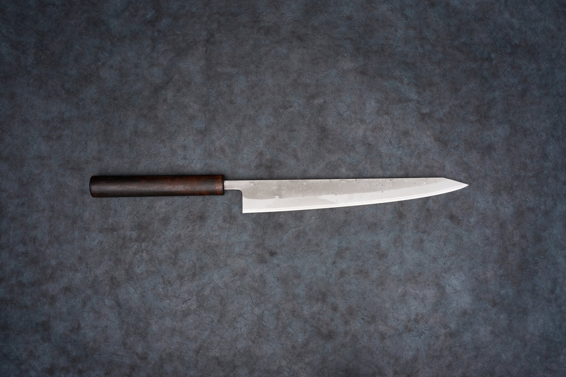 Fujimoto Nashiji Sujihiki 240mm: A sleek Japanese slicing knife with a slender steel blade and dark wooden handle, ideal for precise cuts like sashimi, featuring a carbon steel core with stainless steel protection.