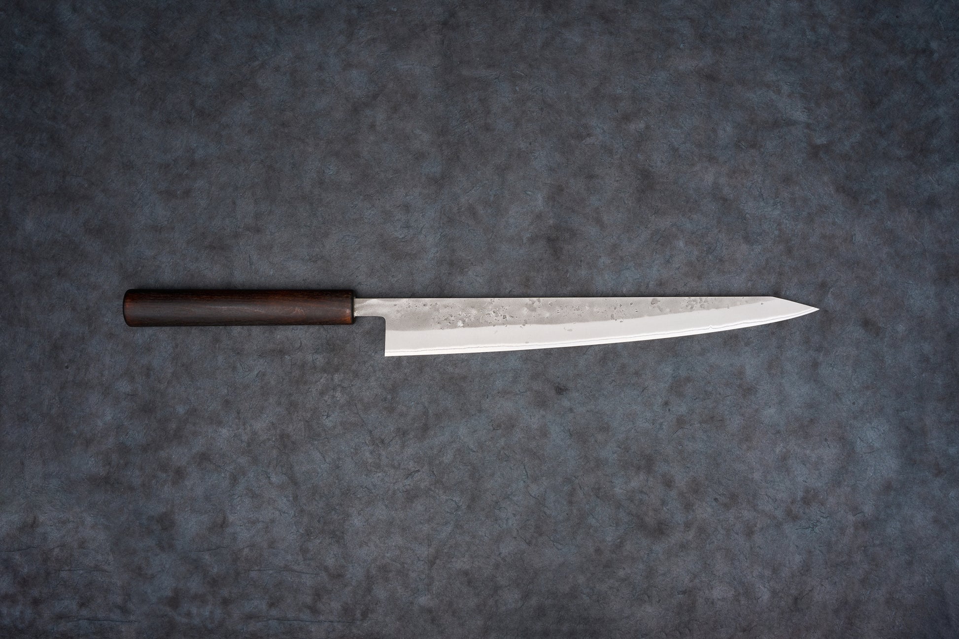 Fujimoto Nashiji Sujihiki 270mm: A slender, polished steel Japanese kitchen knife with a traditional dark wooden handle, perfect for precise slicing of sashimi and delicate meats, showcasing subtle hammer marks.