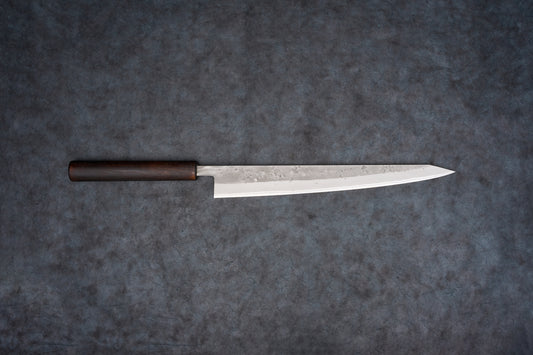 Fujimoto Nashiji Sujihiki 270mm: A slender, polished steel Japanese kitchen knife with a traditional dark wooden handle, perfect for precise slicing of sashimi and delicate meats, showcasing subtle hammer marks.
