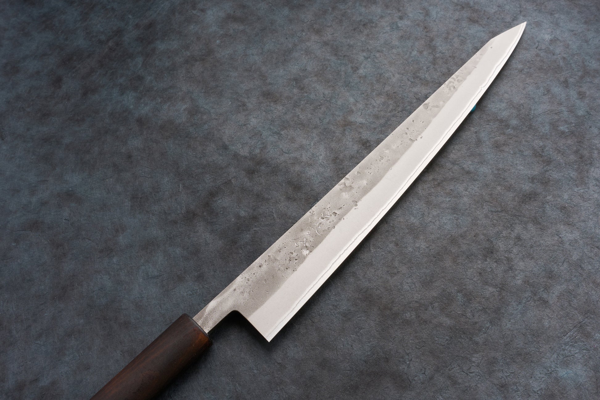 Fujimoto Nashiji Sujihiki 270mm: A sleek, single-edged Japanese slicing knife with a polished steel blade, subtle hammer textures, faint hamon line, and a dark wooden handle, crafted for precision slicing.