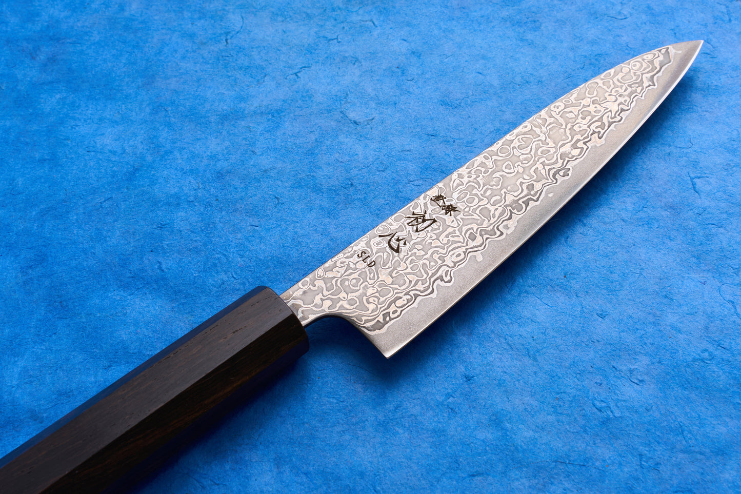 Hatsukokoro SLD Hikari Kurozome Damascus Petty 130mm knife with a patterned steel blade and octagonal dark wood handle, ideal for precise cutting tasks.