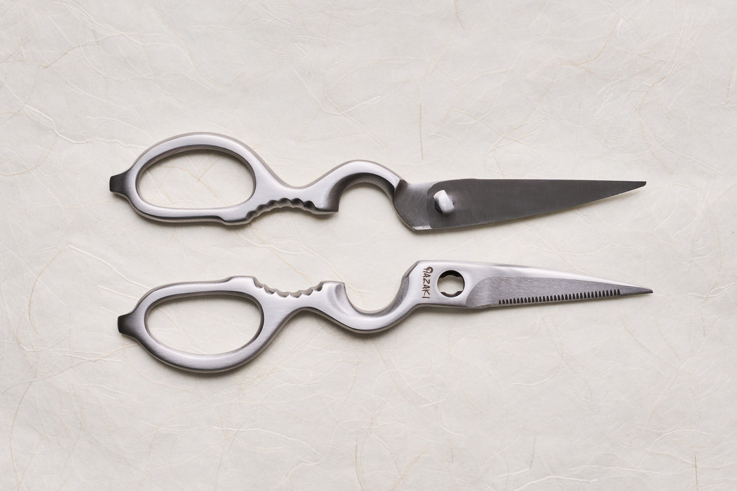 Hazaki Stainless Kitchen Shears, separated into two ergonomic halves with distinct straight and serrated blades, showcasing their versatility in utility tasks, including built-in nutcracker and bottle opener features.