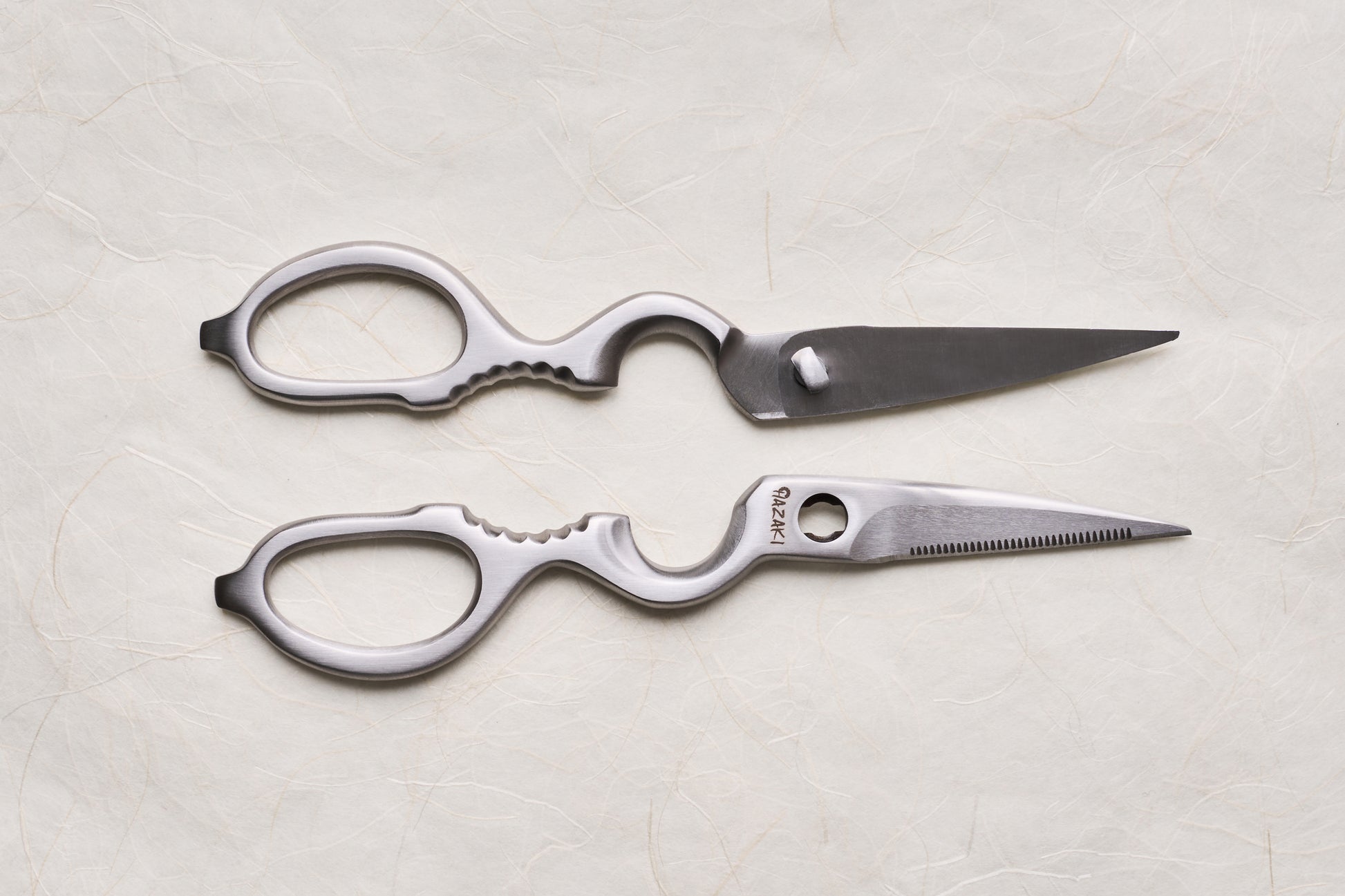Hazaki Stainless Kitchen Shears, separated into two ergonomic halves with distinct straight and serrated blades, showcasing their versatility in utility tasks, including built-in nutcracker and bottle opener features.