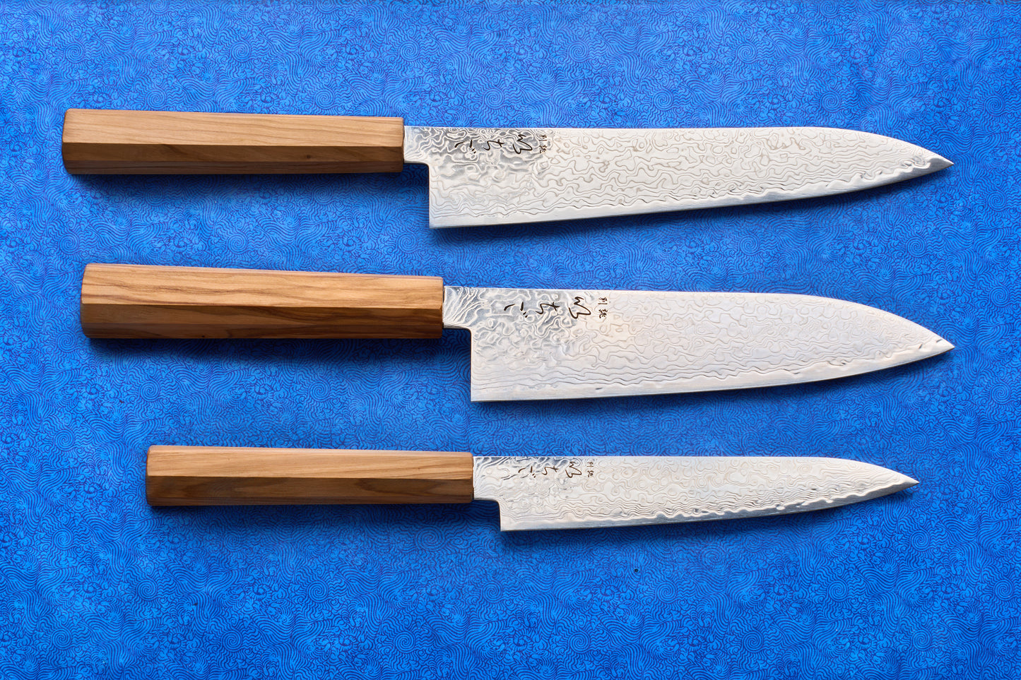 ICHIGO Haku 3 Piece Knife Set featuring Damascus-patterned blades and octagonal wooden handles, embodying traditional Japanese craftsmanship on vibrant fabric. Perfect for culinary enthusiasts.