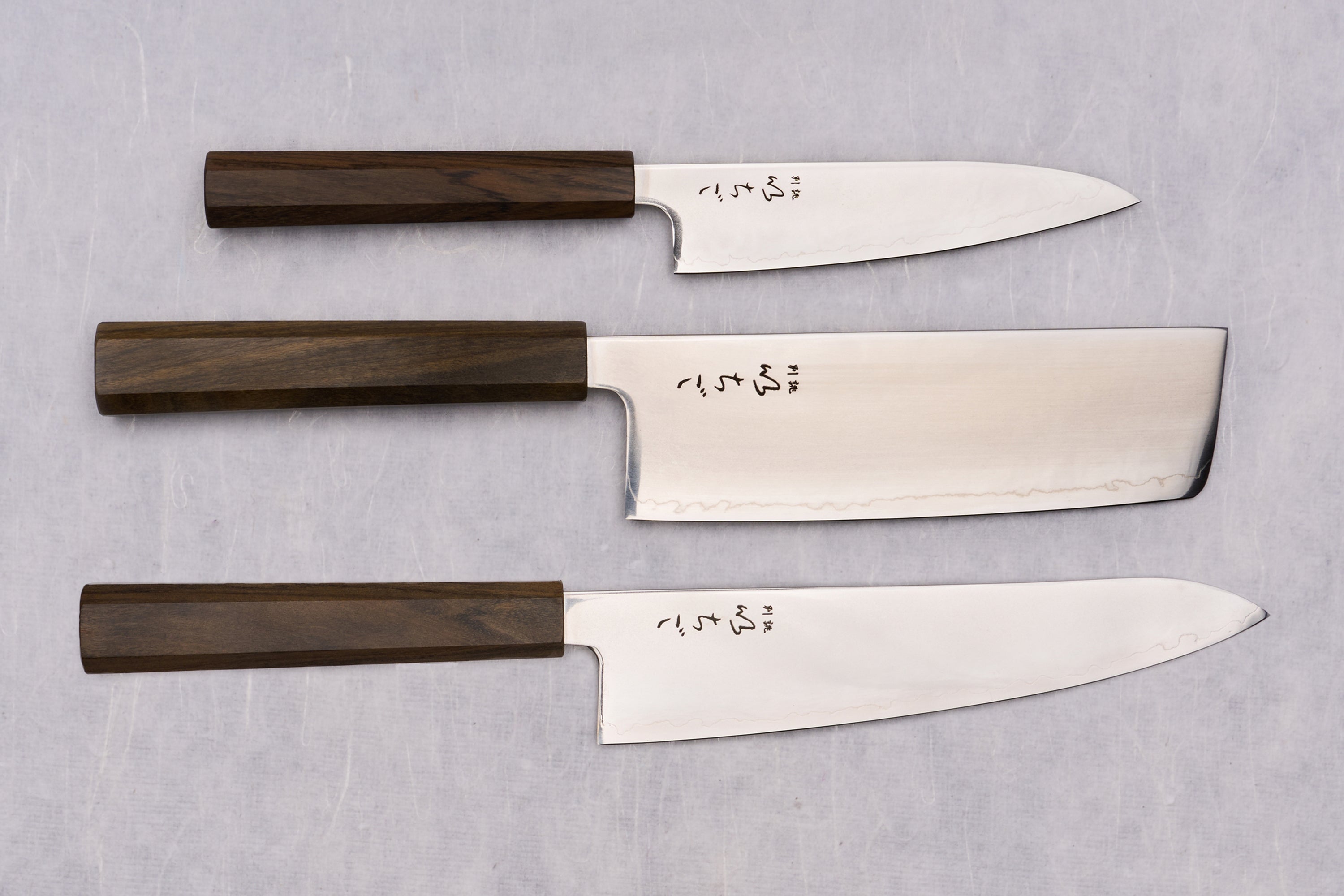 ICHIGO Nezu 3 Piece Knife Set displayed: utility, nakiri, and chef’s knives; polished blades with dark octagonal handles, showcasing Japanese craftsmanship and elegance.