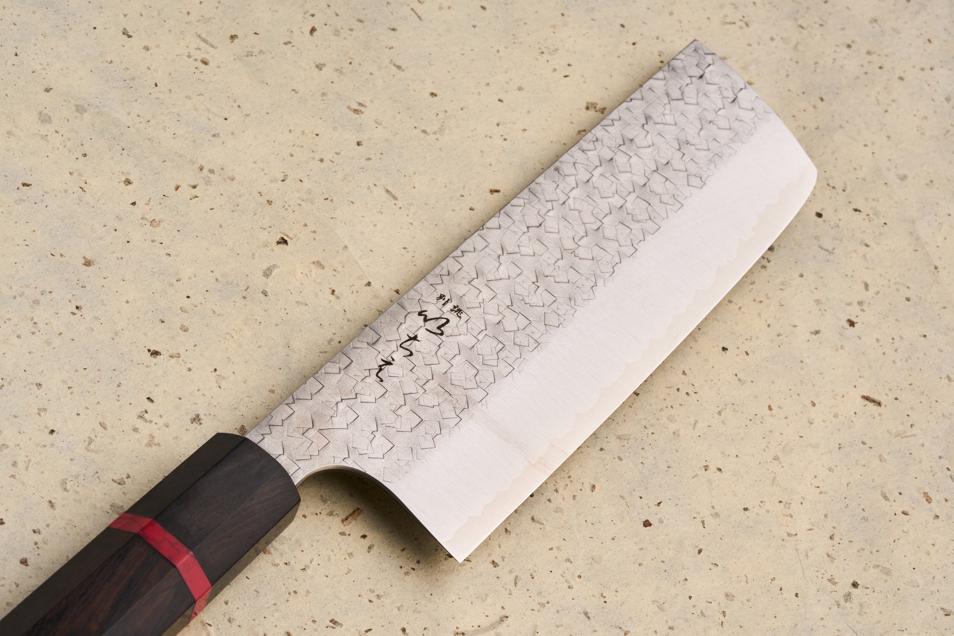 ICHIE x Shibata Knives SG2 Tsuchime Nakiri 165mm features a hammered pattern on the blade's upper half and an octagonal dark wood handle with a red spacer, ideal for precise vegetable chopping.