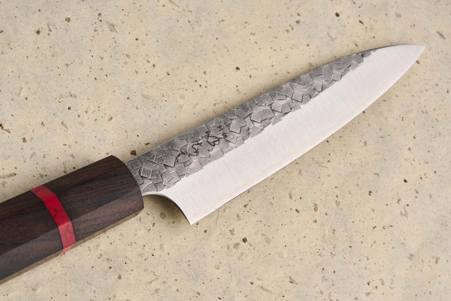 ICHIE x Shibata Knives SG2 Tsuchime Petty 135mm features a hammered blade transitioning to a polished edge, with an octagonal dark wood handle inlaid with a striking red resin band.