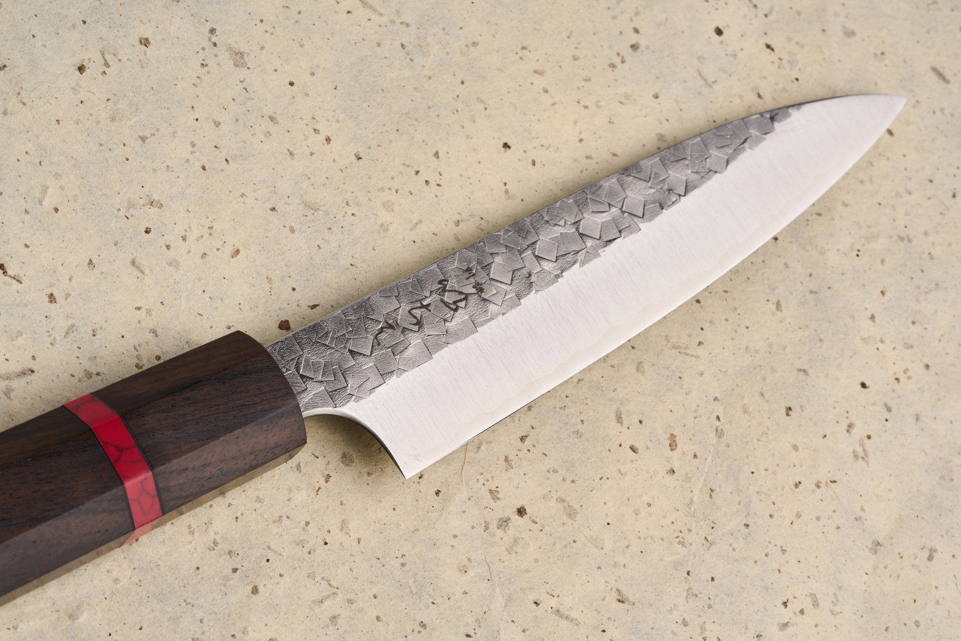 ICHIE x Shibata Knives SG2 Tsuchime Petty 135mm features a hammered blade transitioning to a polished edge, with an octagonal dark wood handle inlaid with a striking red resin band.