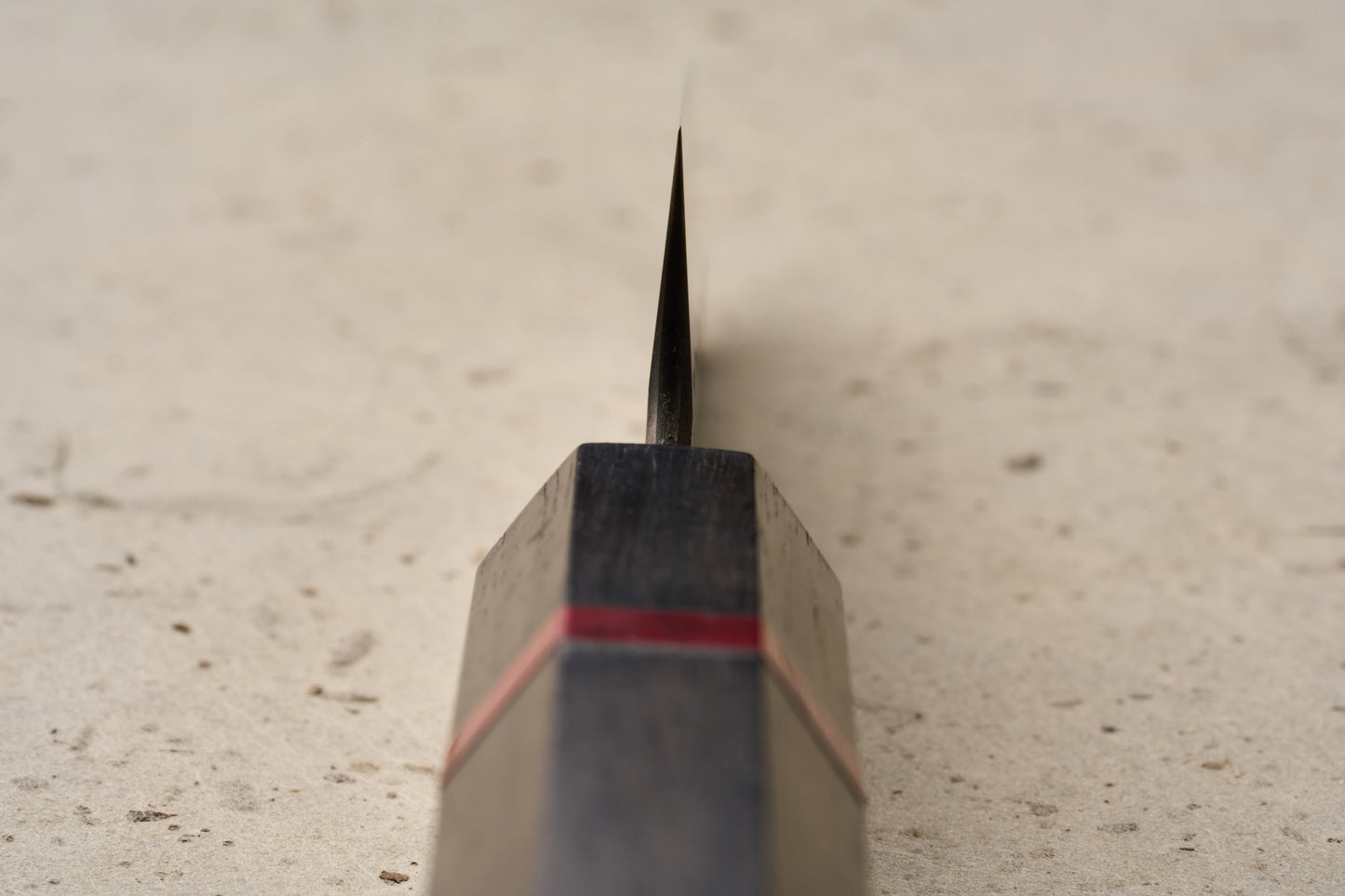 ICHIE x Shibata Knives SG2 Tsuchime Petty 90mm knife with a dark wood handle featuring a red accent band, viewed from handle to blade on a speckled surface, ideal for precise cutting tasks.