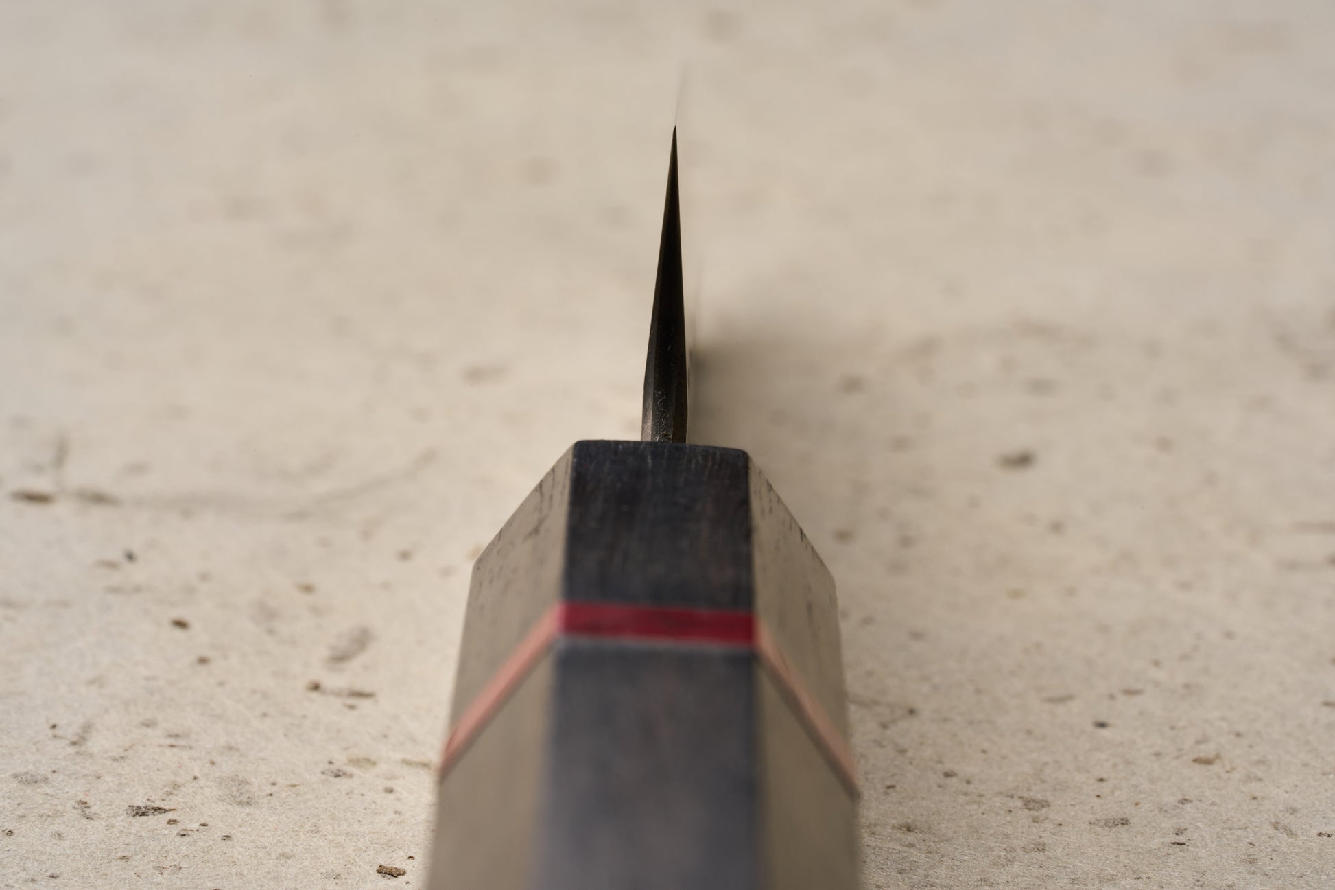 ICHIE x Shibata Knives SG2 Tsuchime Petty 90mm knife with a dark wood handle featuring a red accent band, viewed from handle to blade on a speckled surface, ideal for precise cutting tasks.