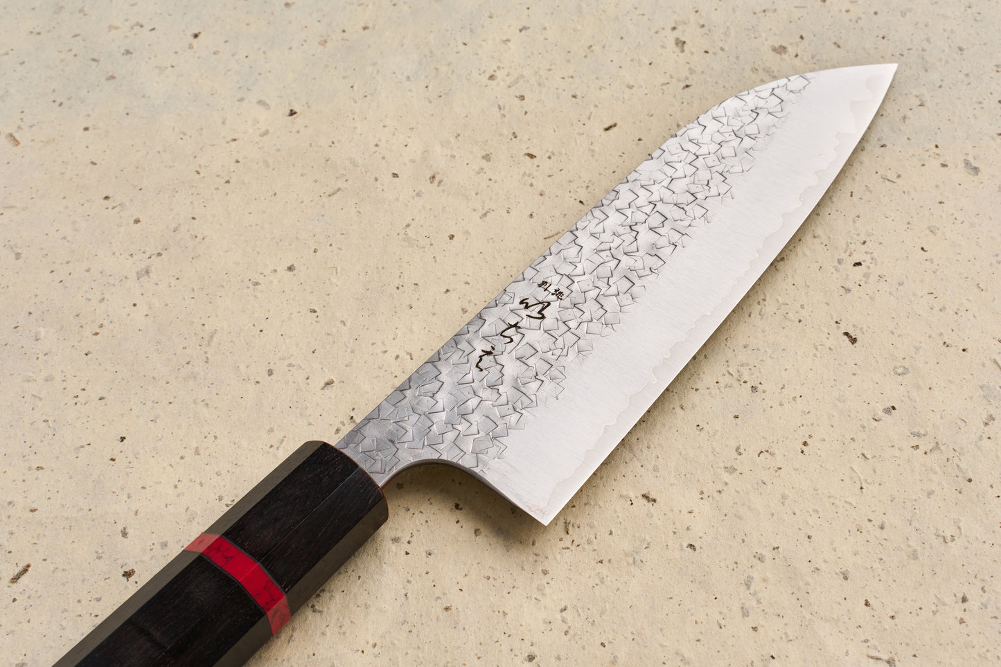 ICHIE x Shibata Knives SG2 Tsuchime Santoku 165mm features a broad, stainless-steel blade with a hammered finish and an octagonal dark wooden handle, embodying Japanese craftsmanship for versatile kitchen use.