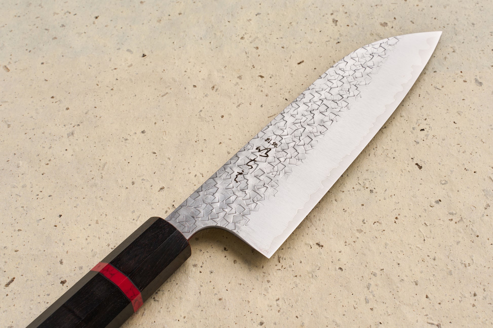 ICHIE x Shibata Knives SG2 Tsuchime Santoku 165mm features a broad, stainless-steel blade with a hammered finish and an octagonal dark wooden handle, embodying Japanese craftsmanship for versatile kitchen use.