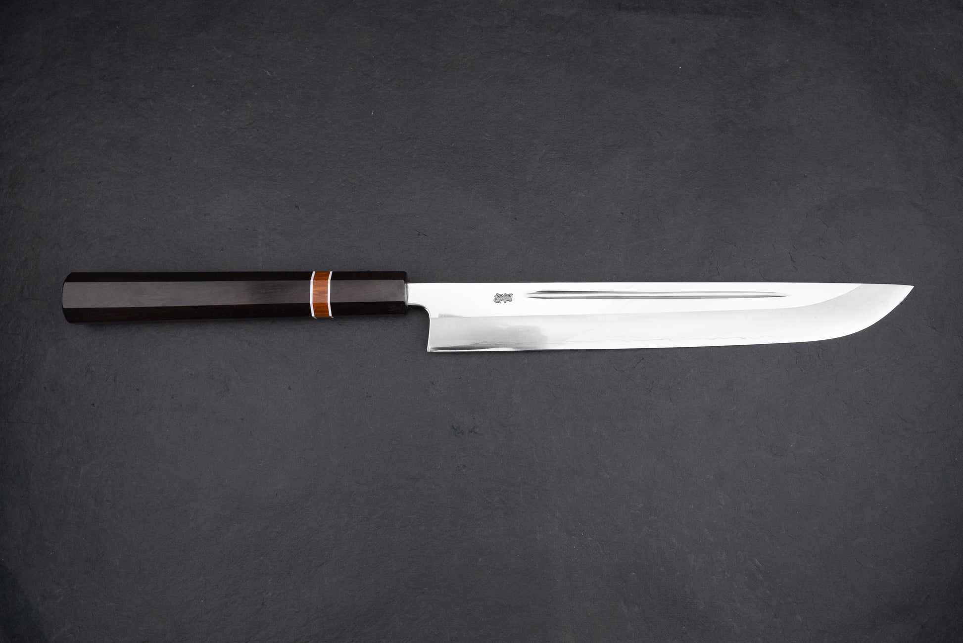 Kurotori Tanzo Ginsan Maguro Bocho, a sleek Japanese slicing knife, features a polished steel blade for precision cuts and a dark octagonal wooden handle, ideal for sashimi preparation.