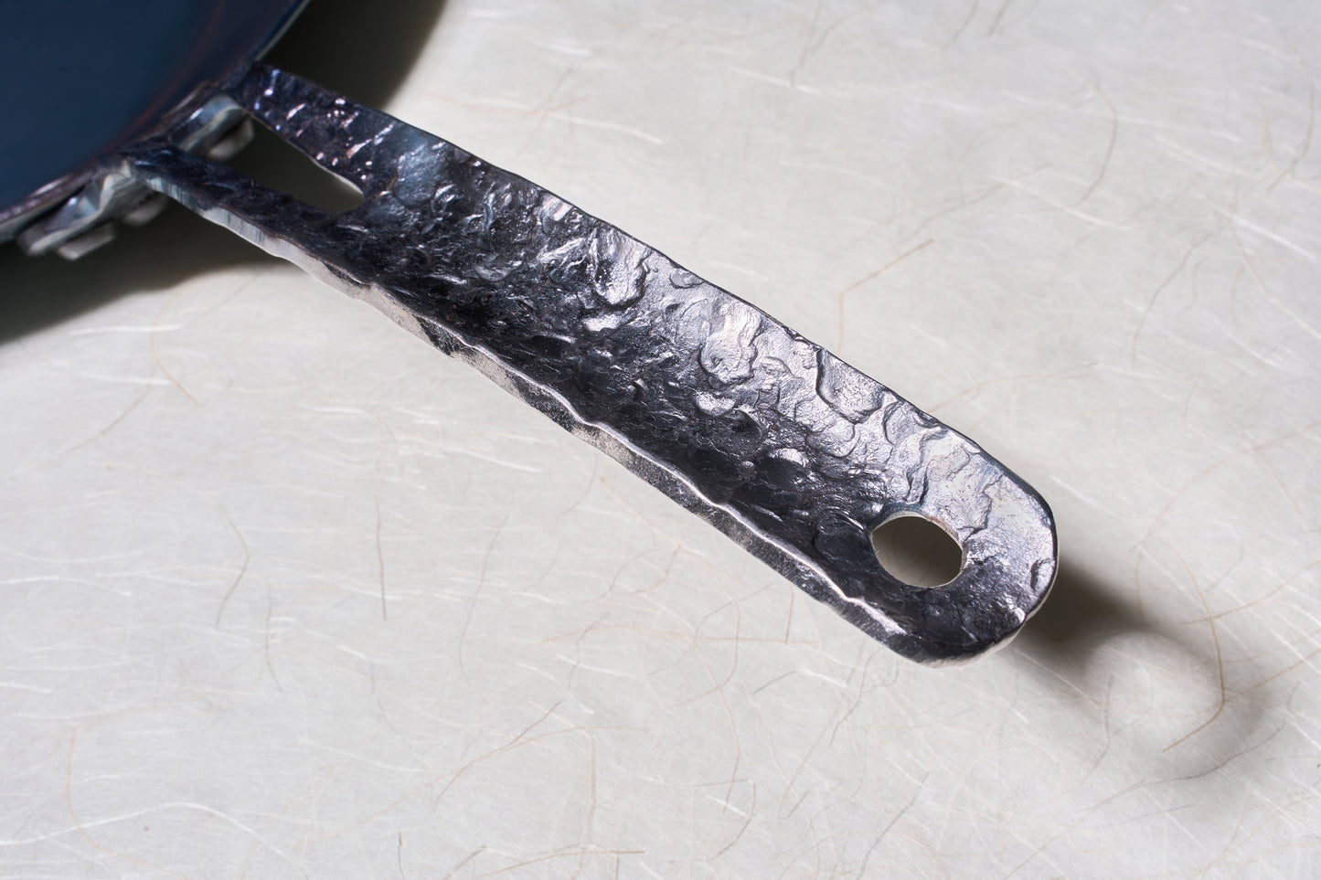 Leechtown Blacksmith Co. Medium Flamerider Carbon Steel Pan features a rugged, hammered-textured handle with attachment slot and hanging hole, showcasing expert craftsmanship.