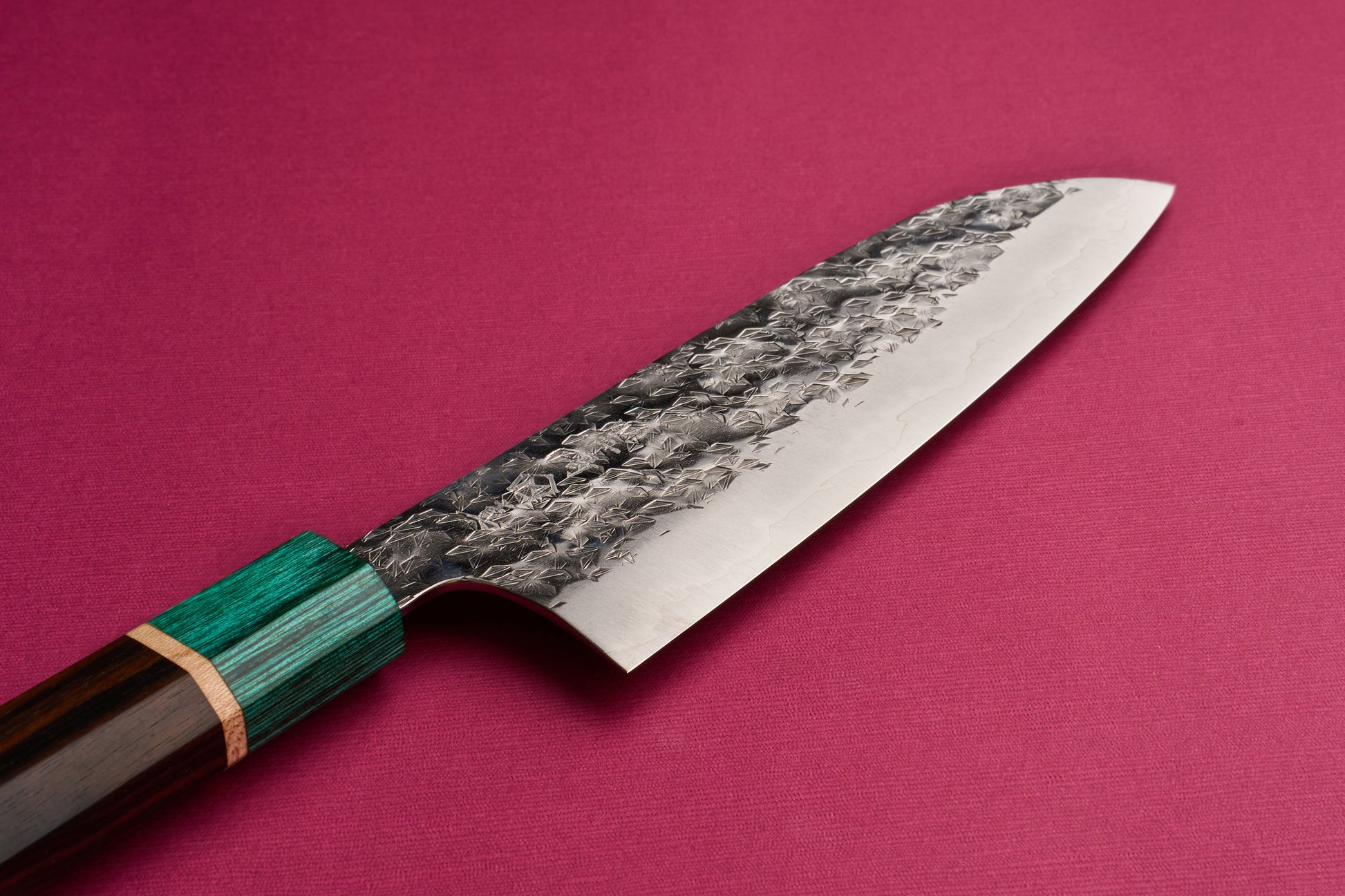 Makoto Kurosaki SPG STRIX Samidorizuki Santoku 165mm features a hammered steel blade and a layered wood handle with a green bolster, presented on reddish-pink fabric, embodying Japanese craftsmanship.