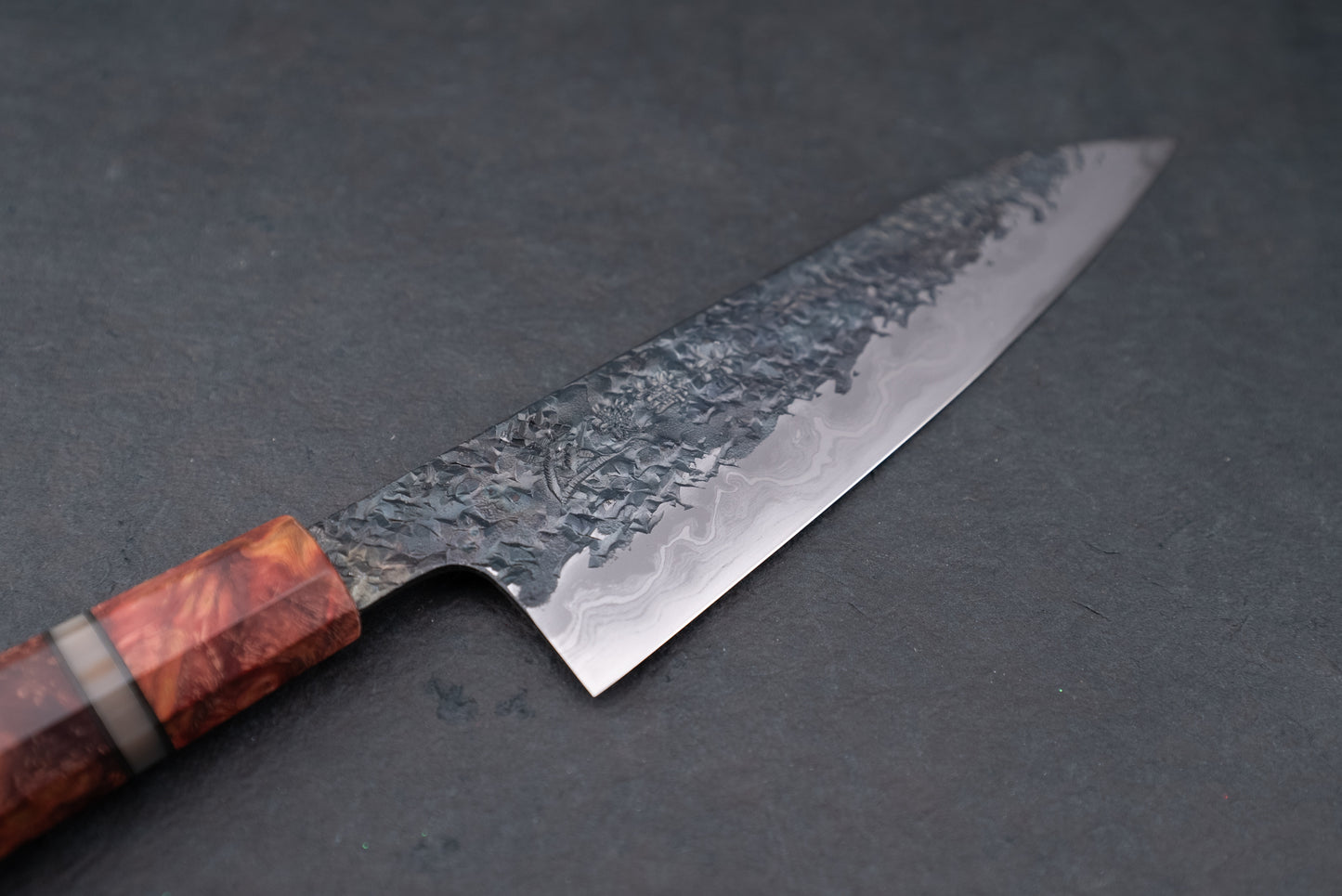 Kisuke Manaka ENN Gyuto 210mm features a hammered steel blade with Damascus pattern, polished edge, and a wooden handle, reflecting exquisite Japanese craftsmanship for culinary enthusiasts.
