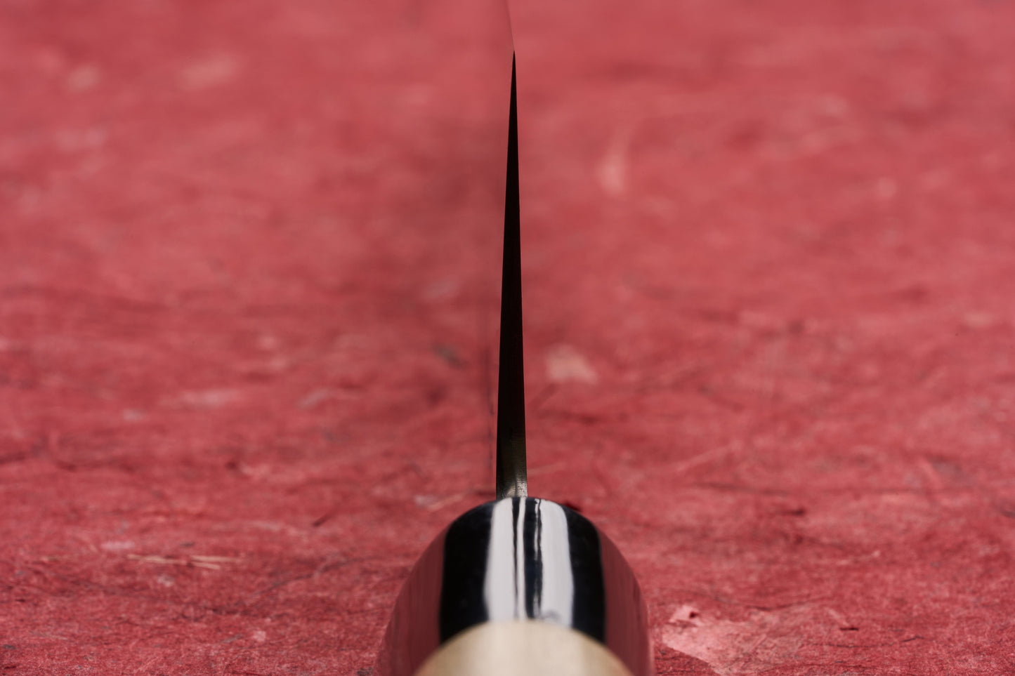 Masamoto KS Hongasumi Gyuto 210mm blade edge close-up, showcasing its extreme thinness and precision against a textured background, with a hint of the handle visible, epitomizing Japanese craftsmanship.