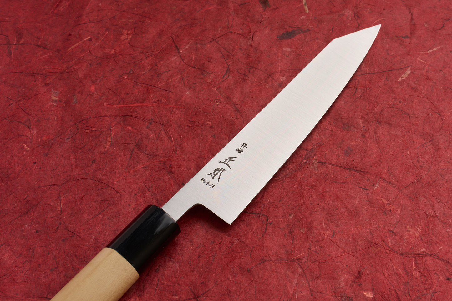 Masamoto KS Hongasumi Kiritsuke Petty 165mm knife with a single-bevel blade and etched Japanese characters, featuring a light wood handle and black ferrule, resting on a red textured surface.