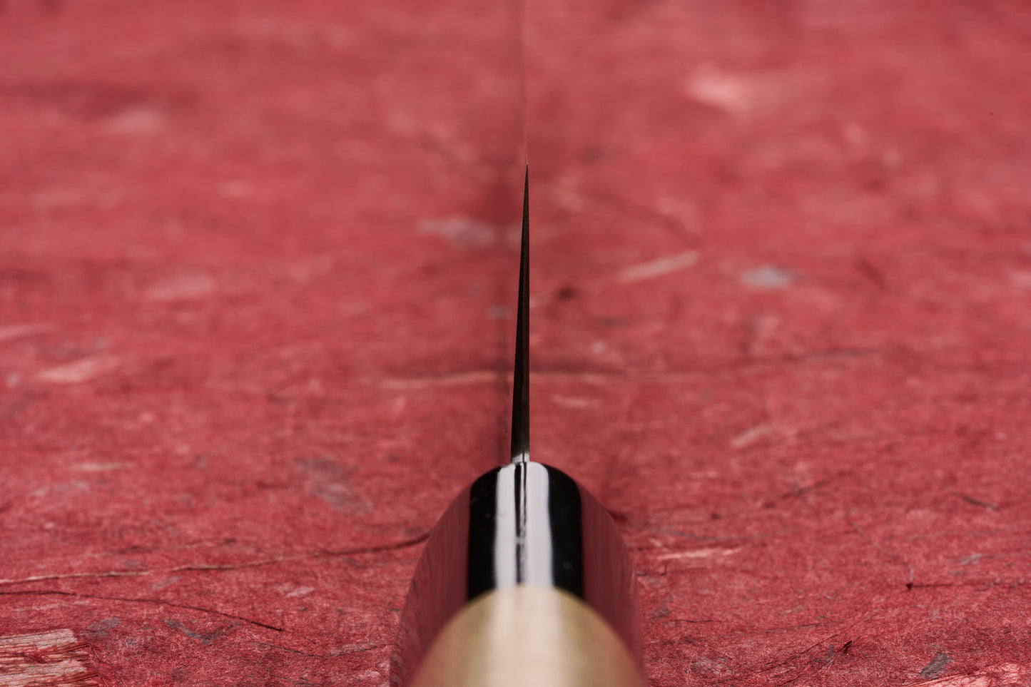 Masamoto KS Hongasumi Kiritsuke Petty 165mm knife blade, viewed edge-on against a textured red surface, showcasing its precision and ultra-thin design, ideal for intricate kitchen tasks.