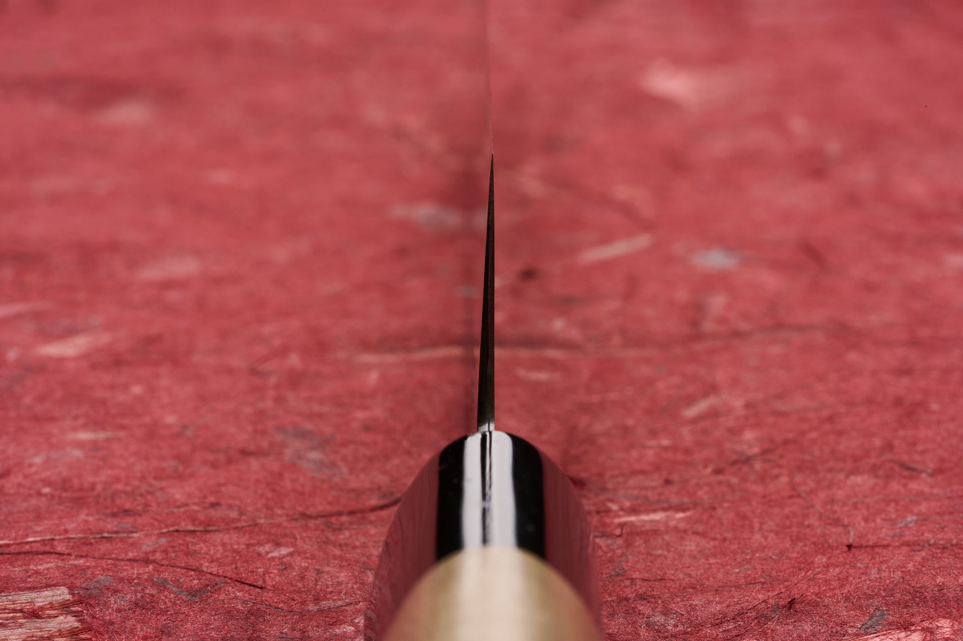 Masamoto KS Hongasumi Kiritsuke Petty 165mm knife blade, viewed edge-on against a textured red surface, showcasing its precision and ultra-thin design, ideal for intricate kitchen tasks.