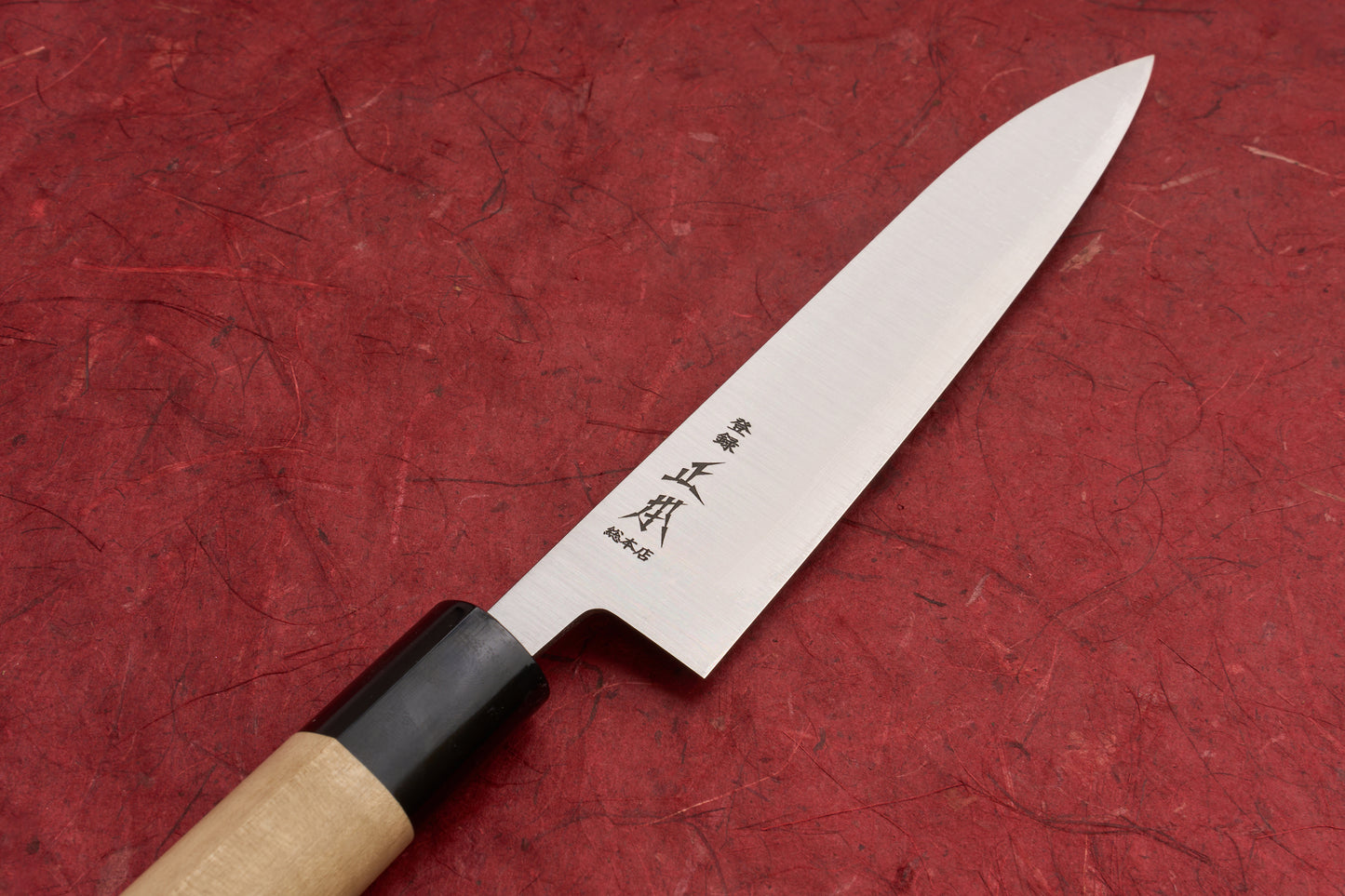 Masamoto KS Hongasumi Petty 165mm knife with a slender stainless-steel blade etched with Japanese characters, rests on a red surface. Features a wooden handle with a dark bolster, ideal for precision tasks.