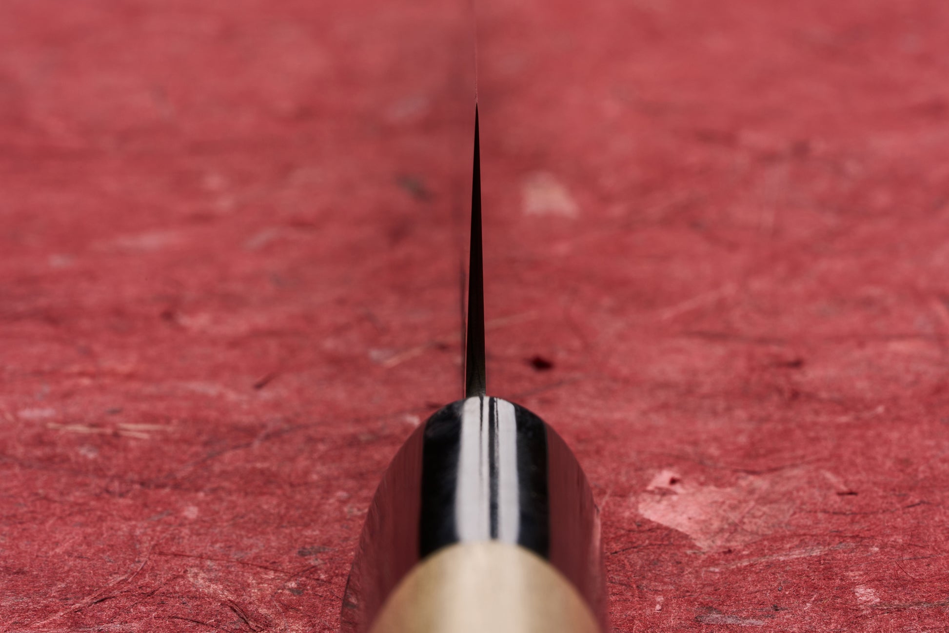 Masamoto KS Hongasumi Petty 165mm knife blade, captured in an edge-on close-up against a red textured background, showcases its precision and thinness, ideal for detailed kitchen tasks.
