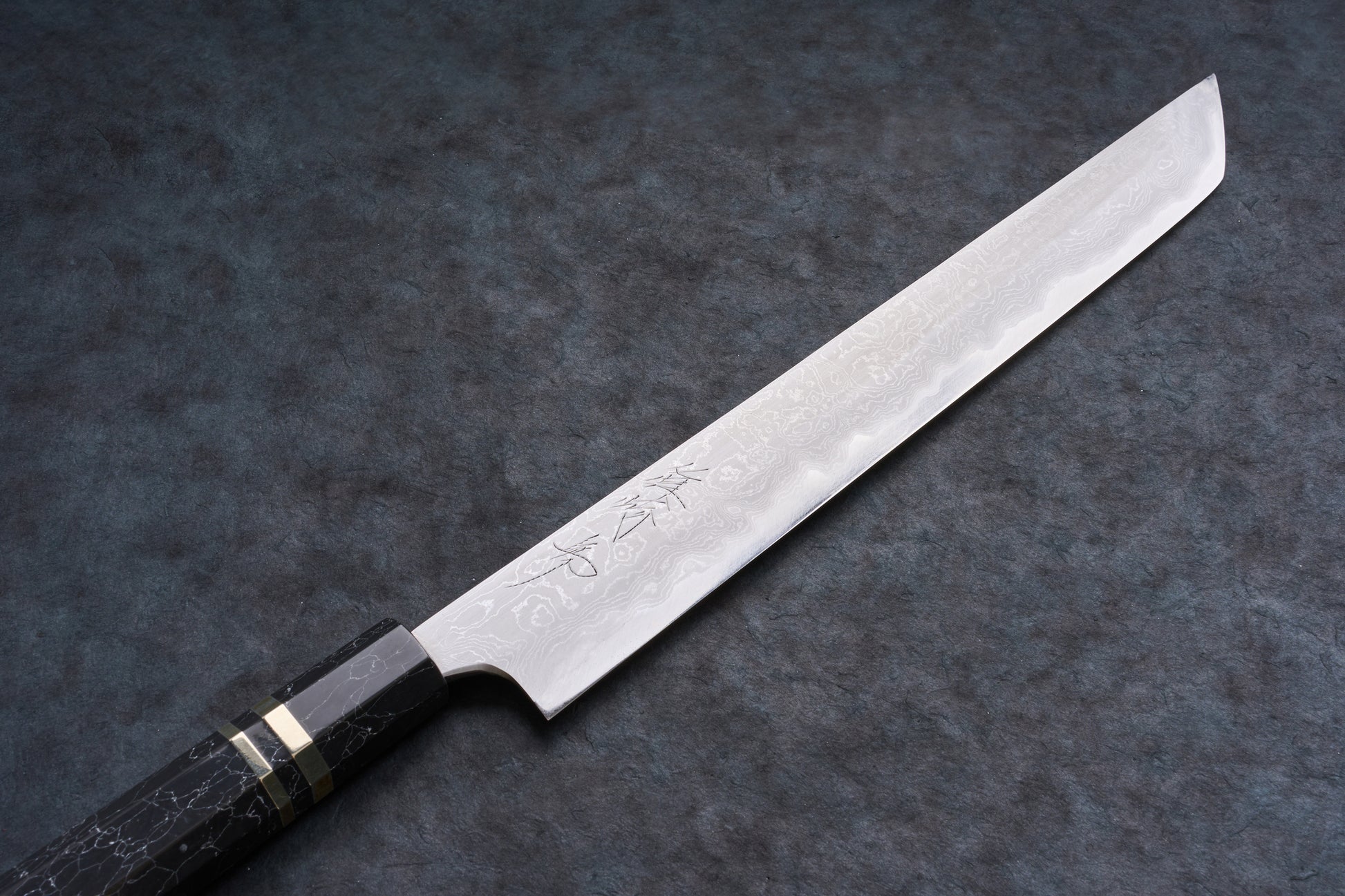 Mazaki Aogami Super Honsanmai Damascus Sakimaru Sujihiki 300mm knife with patterned Damascus steel, etched kanji, and a black octagonal handle with brass bands.