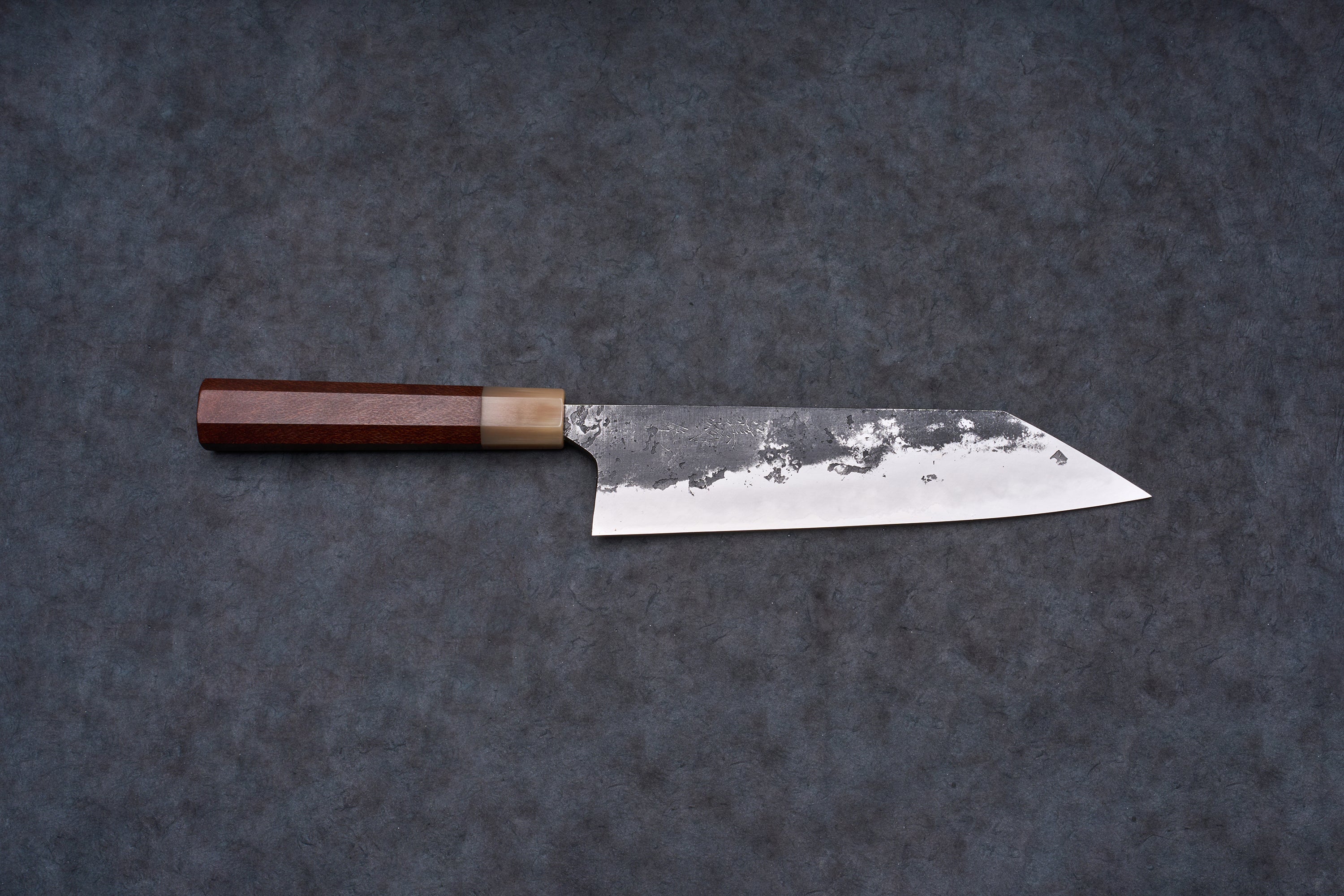 Mazaki Aogami Super Honsanmai Kurouchi Nashiji Kiritsuke Gyuto 210mm, a Japanese-style knife with a broad steel blade and octagonal wooden handle, displayed on a dark surface.