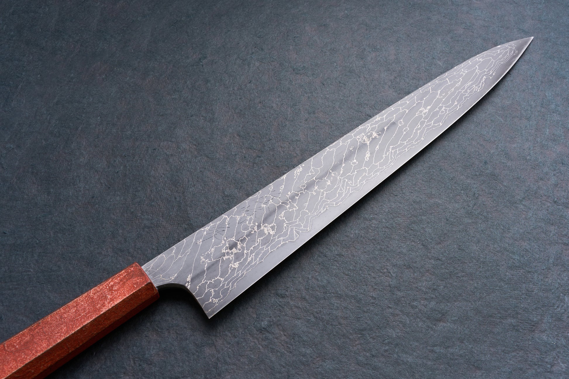 Mazaki Aoichi Beads Black Damascus Sujihiki 300mm, a Japanese slicing knife with a patterned blade and reddish wooden handle, on a dark surface.