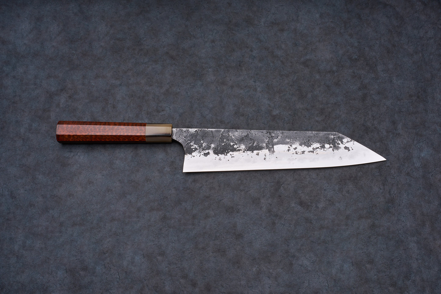 Mazaki Aoichi Honsanmai Kurouchi Nashiji Kiritsuke Gyuto 240mm with a hammered blade and octagonal wooden handle displayed on a textured surface.