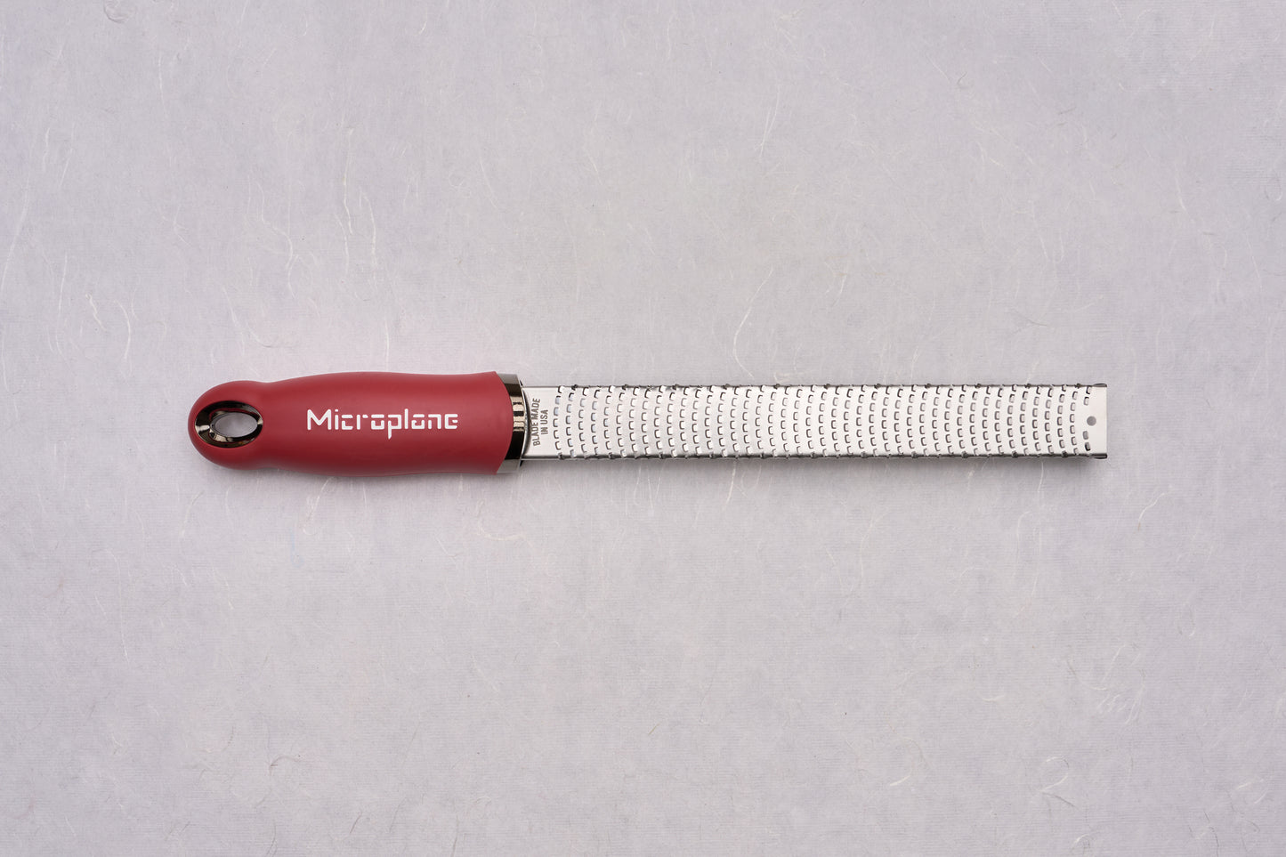 Microplane Premium Classic Zester with a stainless-steel blade featuring sharp teeth, ideal for zesting and grating. Its ergonomic red handle ensures precision, embodying craftsmanship appreciated by both home cooks and professional chefs.
