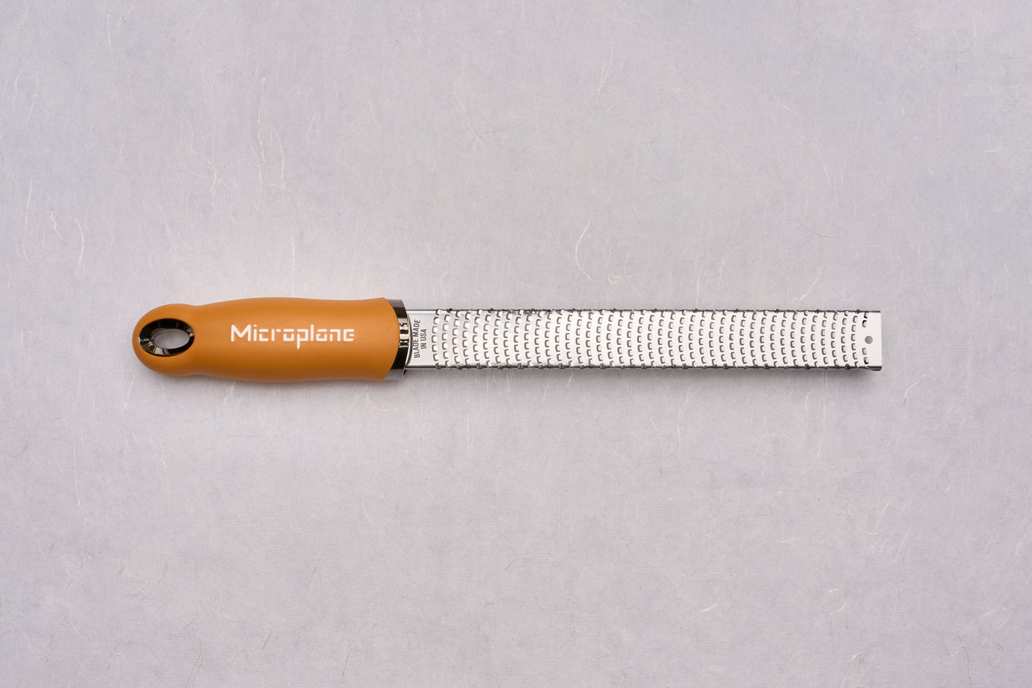 Microplane Premium Classic Zester with a stainless-steel rasp blade and orange handle, ideal for precision zesting and grating, reflecting Knifewear's dedication to quality chef tools.