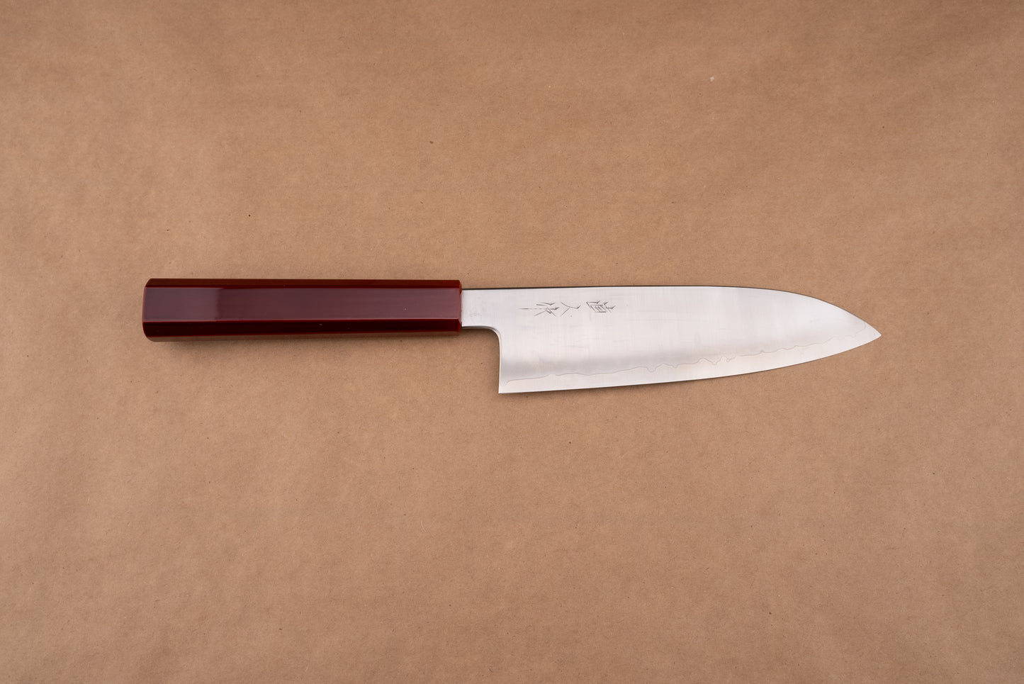 Naohito Myojin Cobalt Special Santoku 180mm showcased on a brown-kraft-paper background, featuring a polished steel blade with a subtle hamon line and a glossy, deep-red octagonal handle.