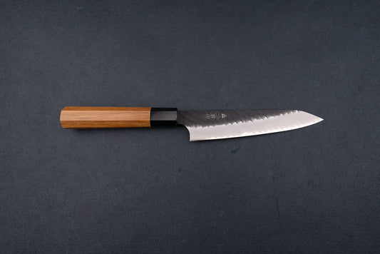 Nigara SG2 Kurouchi Tsuchime Petty 150mm knife features a long, gently curved blade with a hammered finish and an octagonal wooden handle, ideal for precise cutting tasks.